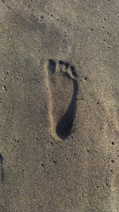 L'impronta di un piede nudo impressa sulla sabbia bagnata del mare, simbolo di un ricordo d'estate che resta.