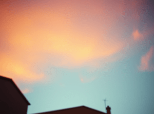 Un cielo celestino sfumato dalla luce calda del tramonto, con una nuvola leggera e il profilo di un tetto, simbolo di una presenza che abita il quotidiano.